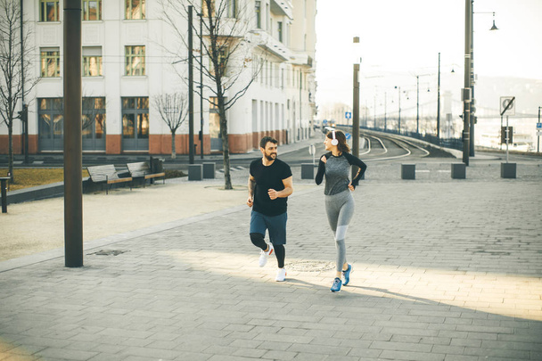 Healthy young couple running in the city with cityscape in background - Photo, Image