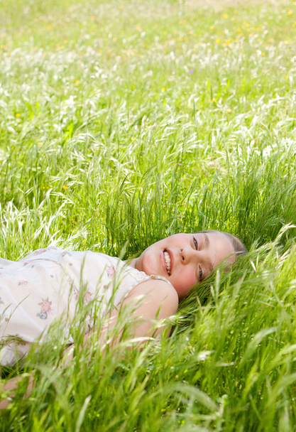 Young teenager laying down on a long green grass garden, smiling at the camera. - Photo, Image