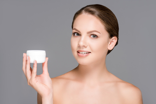 portrait of beautiful young woman holding face cream isolated on grey - Фото, изображение