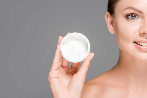 cropped shot of smiling woman holding face cream in jar isolated on grey - Fotoğraf, Görsel