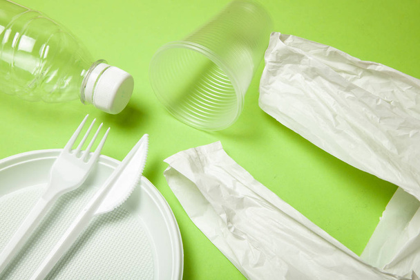Utensili monouso in plastica su verde. forchetta, coltelli, piatti, tazze e un pacchetto, bottiglia, borsa
 - Foto, immagini