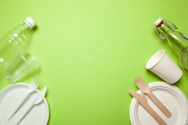 Пластиковая и экологически чистая одноразовая посуда из бамбуковой древесины и бумаги на зеленом фоне. вилка, ножи, тарелки, чашки и бутылки
 - Фото, изображение