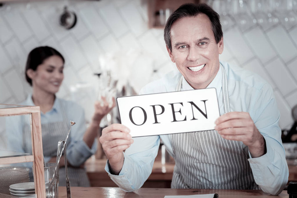 Excited waiter smiling and holding the open sign - Fotoğraf, Görsel