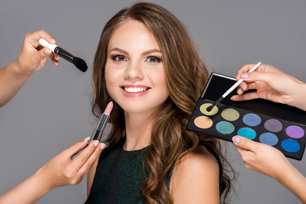 partial view of makeup artists with cosmetics and beautiful smiling woman isolated on grey - 写真・画像