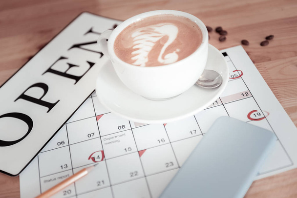 Laconic photo of a cup of coffee and a sign open on a calendar - Fotó, kép