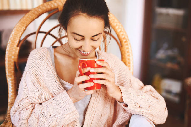 Soft photo of woman in a wicker chair with cup of coffee. Woman wearing in cozy knitted pink sweater. - Photo, Image