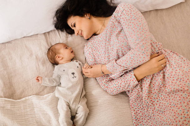 Happy young mother with little baby boy on bed  - Фото, зображення