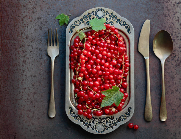 Redcurrants on a metal dish with fork , spoon and knife. Concept for healthy eating, dieting and antioxidant. Top view. - Photo, Image