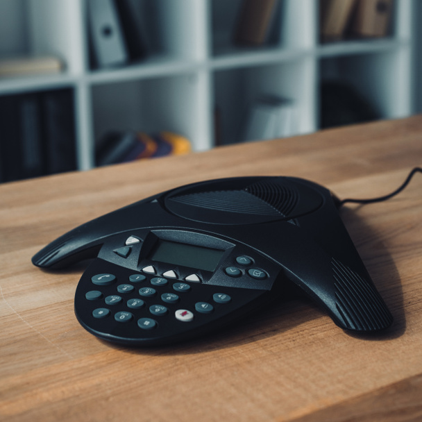 speakerphone on wooden table at office with blurred bookshelves on background - Foto, Bild