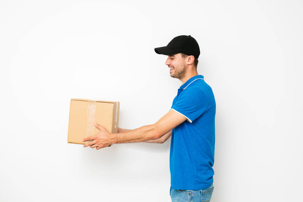 delivery man standing in profile and offering the mail, or package cardbox, to someone, on white background - Photo, image