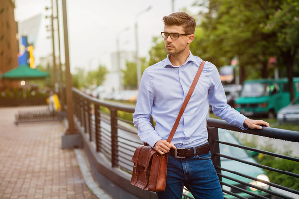 going home after office. handsome smart casual man with eyeglasses and leather bag walking outside after work - Фото, изображение