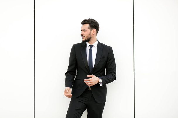 elegant man in suit, businessman, presenter, standing on white wall interacting with free space aroiund him, presenting something - Foto, immagini