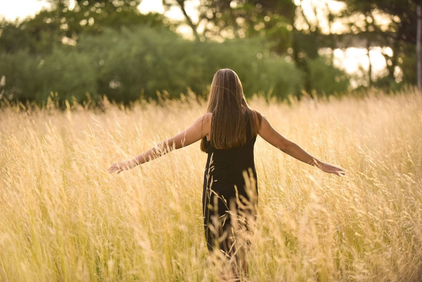 jonge vrouw met uitgestrekte armen op wilde velden - Foto, afbeelding