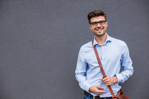 pointing the empty side. handsome smart casual man with eyeglasses and leather bag outside pointing a free space next to him with confidence and smile - Zdjęcie, obraz
