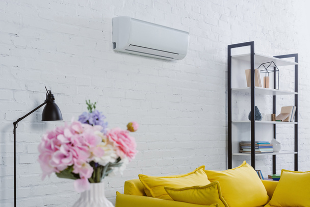 interior of modern living room with flowers in vase, yellow couch and air conditioner hanging on white wall - 写真・画像