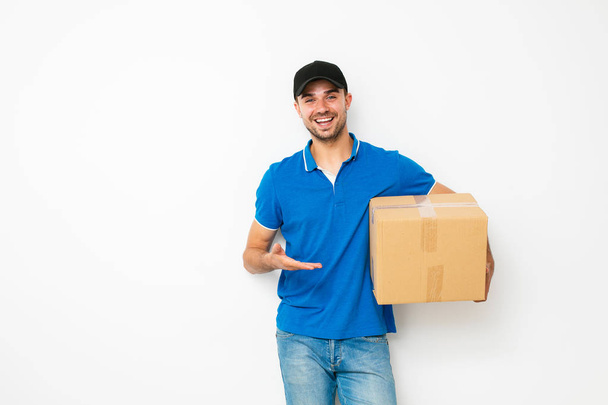 your shipping is here. delivery man in blue shirt standing politely and pointing his cardbox, on white background - Φωτογραφία, εικόνα