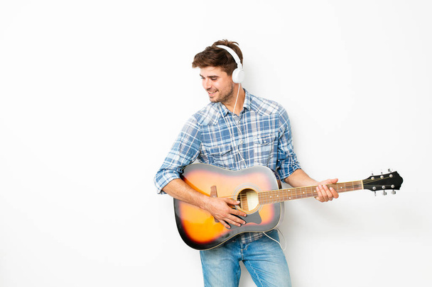 hobby for boys. man playing the guitar with headsets on his head, enjoying his spare time in his own house, doing what he likes, on white background - Photo, image