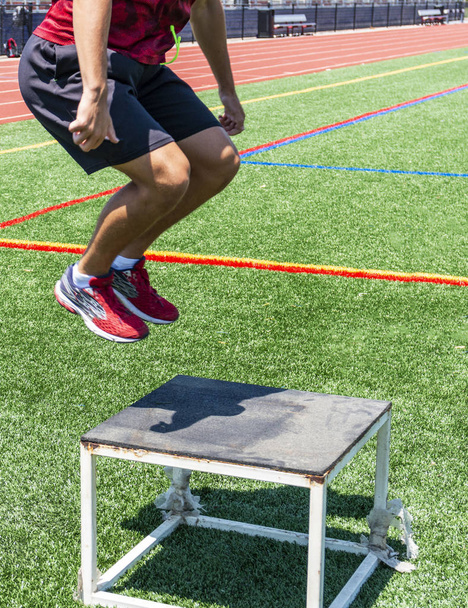 A track and field athlete perfoming plyometric box jumps outside on a green turf field. - Photo, Image