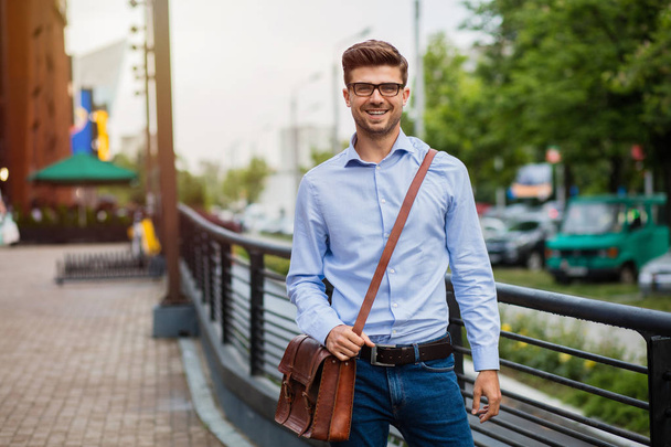 going home after office. handsome smart casual man with eyeglasses and leather bag walking outside after work - Photo, image