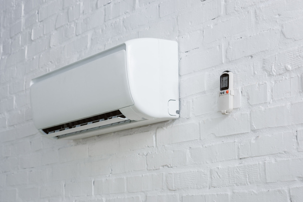 кондиционер висит на стене из белого кирпича с дистанционным управлением
 - Фото, изображение