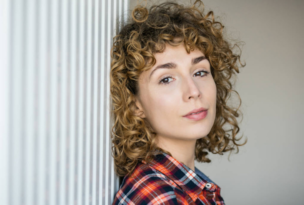 young natural curly woman smiling to camera casual dressed in a checkered shirt inside a house - Valokuva, kuva