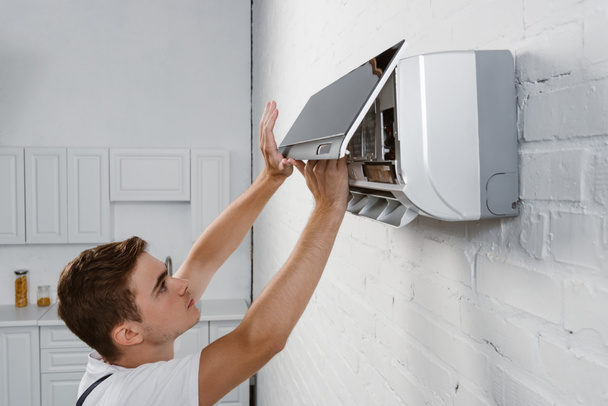 repairman taking off dirty filter from air conditioner hanging on white brick wall - Foto, Bild