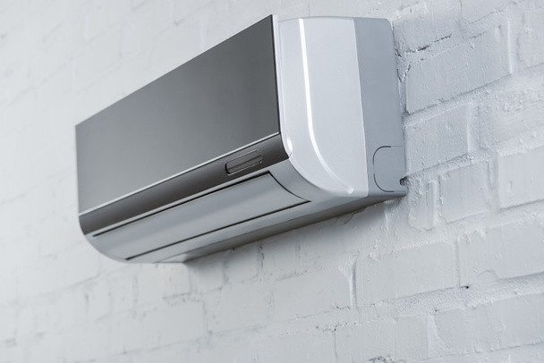 close-up shot of grey air conditioner hanging on white brick wall - Foto, Bild