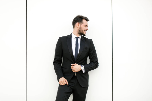 elegant man in suit, businessman, presenter, standing on white wall interacting with free space aroiund him, presenting something - Fotó, kép