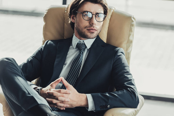 komea huomaavainen liikemies istuu nojatuolissa ja katselee pois moderni toimisto
 - Valokuva, kuva