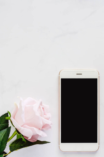 Смартфон со сладкой розовой розой на белом мраморном фоне для медиа-технологий и современной концепции образа жизни (вертикальное изображение
) - Фото, изображение