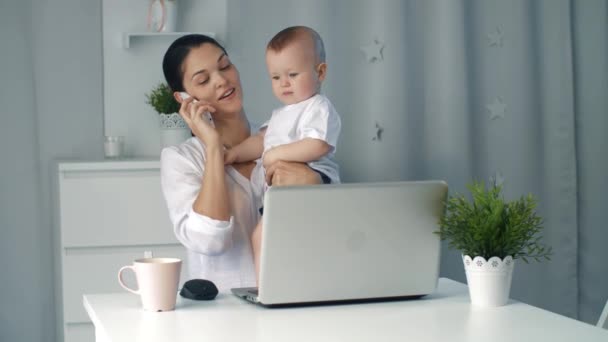 Young mother holding baby while working in home office - Imágenes, Vídeo