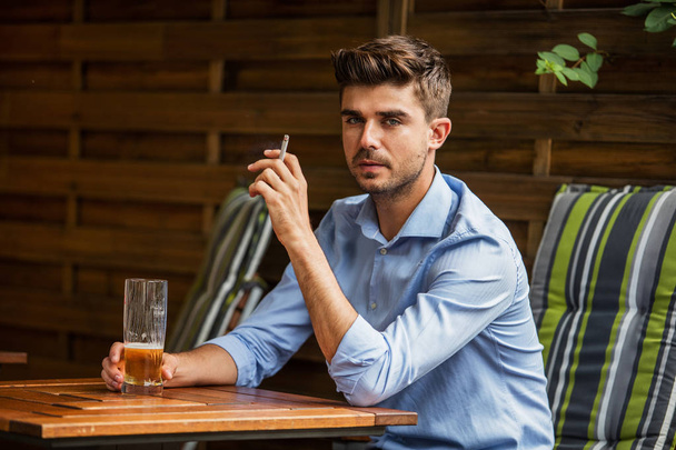 outside smoking. young man, smart casual dressed, smoking cigar outside restaurant on terrace - Foto, Imagen