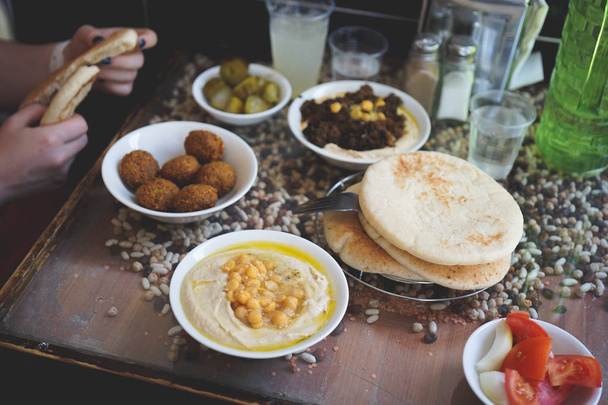 Having an Israeli lunch at cafe in Jerusalem, Israel. Falafels on a plate, creamy hummus with whole cheakpeas, pile of pitas and pickles on the background - Photo, Image