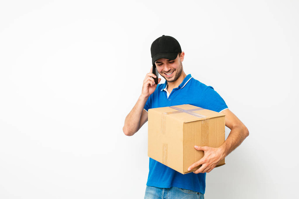 fast delivery. happy delivery man talking at mobile phone with the client who need to deliver his package, isolated on white - Fotografie, Obrázek