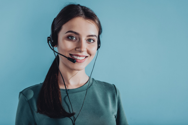 attraktive lächelnde Callcenter-Mitarbeiterin blickt vereinzelt in die Kamera auf blauem Grund - Foto, Bild