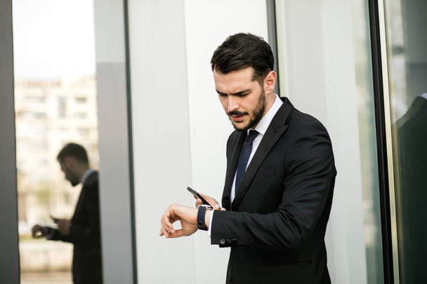 busy elegant businessman looking at his hand watch with mobile phone in  hands, outside - Fotoğraf, Görsel
