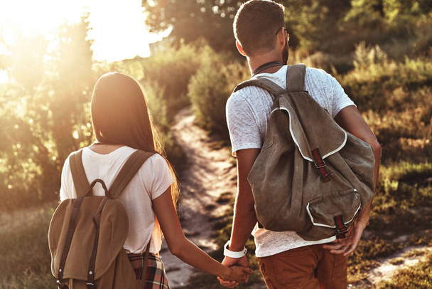 Rear view of young couple with backpacks holding hands while standing outdoors - Fotoğraf, Görsel