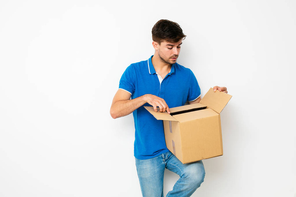 curious man looking inside a cardboard box he holds in his hands on a white background - Foto, imagen