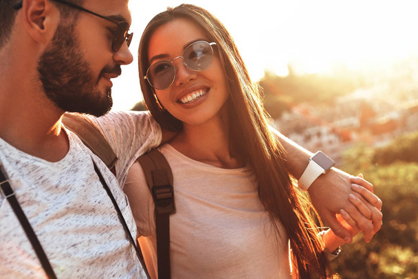 beautiful young couple embracing and smiling while spending time outdoors at sunset  - Photo, image