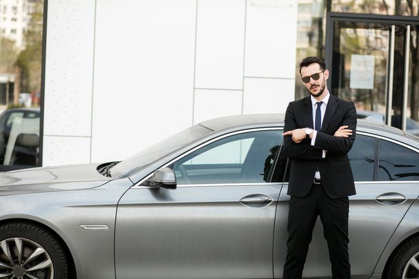 elegant businessman standing outside with folded arms, private driver waiting for his boss pointing limousine - 写真・画像