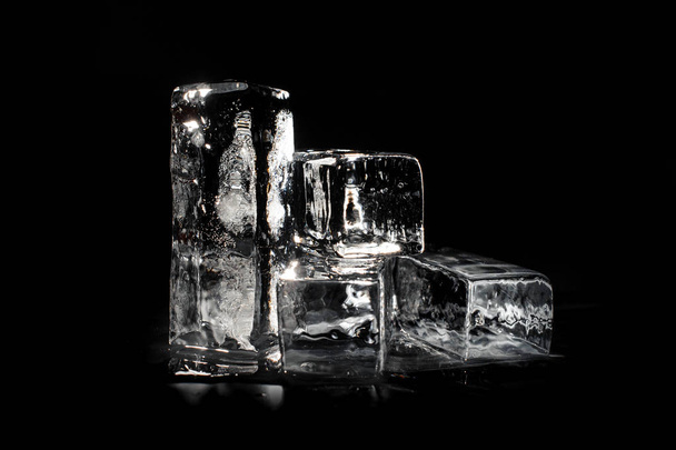 Four clear transparent ice cubes isolated on the black background shining under the light spot - Фото, изображение