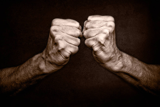 Photo en noir et blanc de poings d'homme âgé sur fond noir, symbolisant la protection et la défense, mais aussi l'attaque et l'agressivité
 - Photo, image