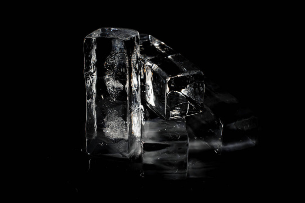 Four clear transparent ice cubes isolated on the black background shining under the directional beam of light - Fotó, kép