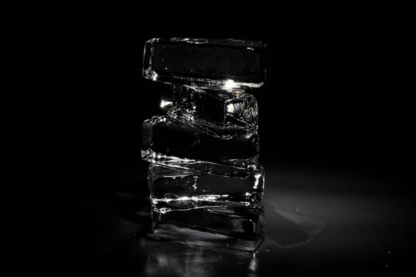 Four clear transparent ice blocks isolated on the black background shining under the light spot - Φωτογραφία, εικόνα