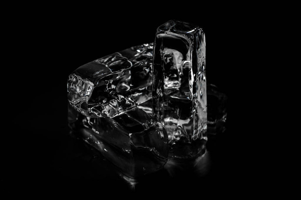 Quattro blocchi di ghiaccio trasparenti sciolti isolati sul fondo nero che brillano sotto il punto luce
 - Foto, immagini