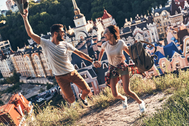 Playful happy young couple in casual clothing jumping and smiling while spending carefree time outdoors - Fotoğraf, Görsel