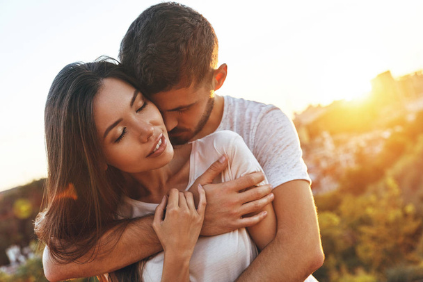 beautiful young couple embracing outdoors, man hugging woman - 写真・画像