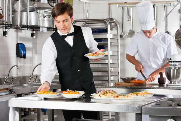 Waiter And Chef Working In Commercial Kitchen - Zdjęcie, obraz