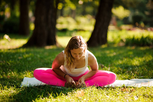 Young woman doing yoga exercises on the grass in a green summer park on sunny day - Fotografie, Obrázek