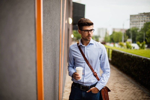 take away coffee .handsome smart casual man with eyeglasses and leather bag outside with a paper cup of coffee on the way to office - Foto, Imagen